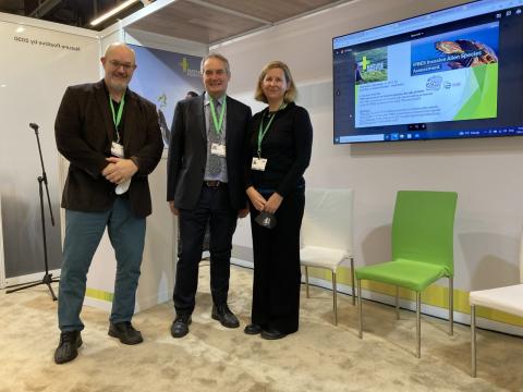 Three people standing beside a large monitor screen